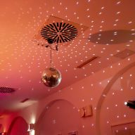 Diskokugel an der Decke, die Lichtmuster in einem rötlich beleuchteten Raum wirft.